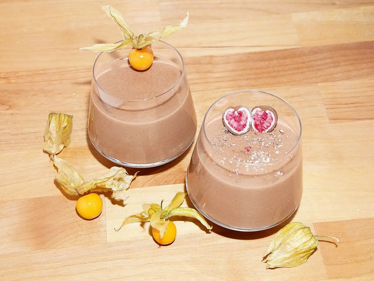 Dos vasitos de mousse de chocolate con frambuesa liofilizada sobre una tabla de madera