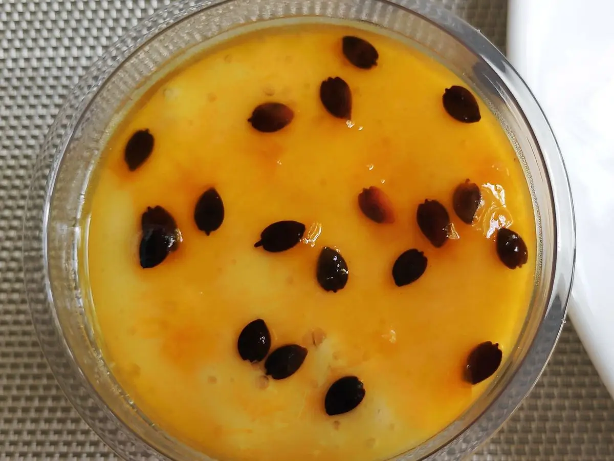 Recipiente de cristal con mousse de maracuyá anaranjada salpicada de semillas negras