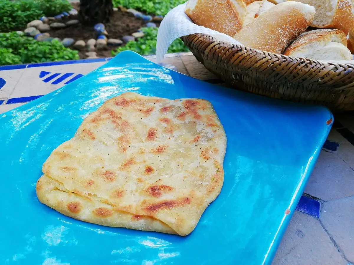 Msemen marroquí relleno, torta cuadrada plegada y dorada, servida sobre un plato azul