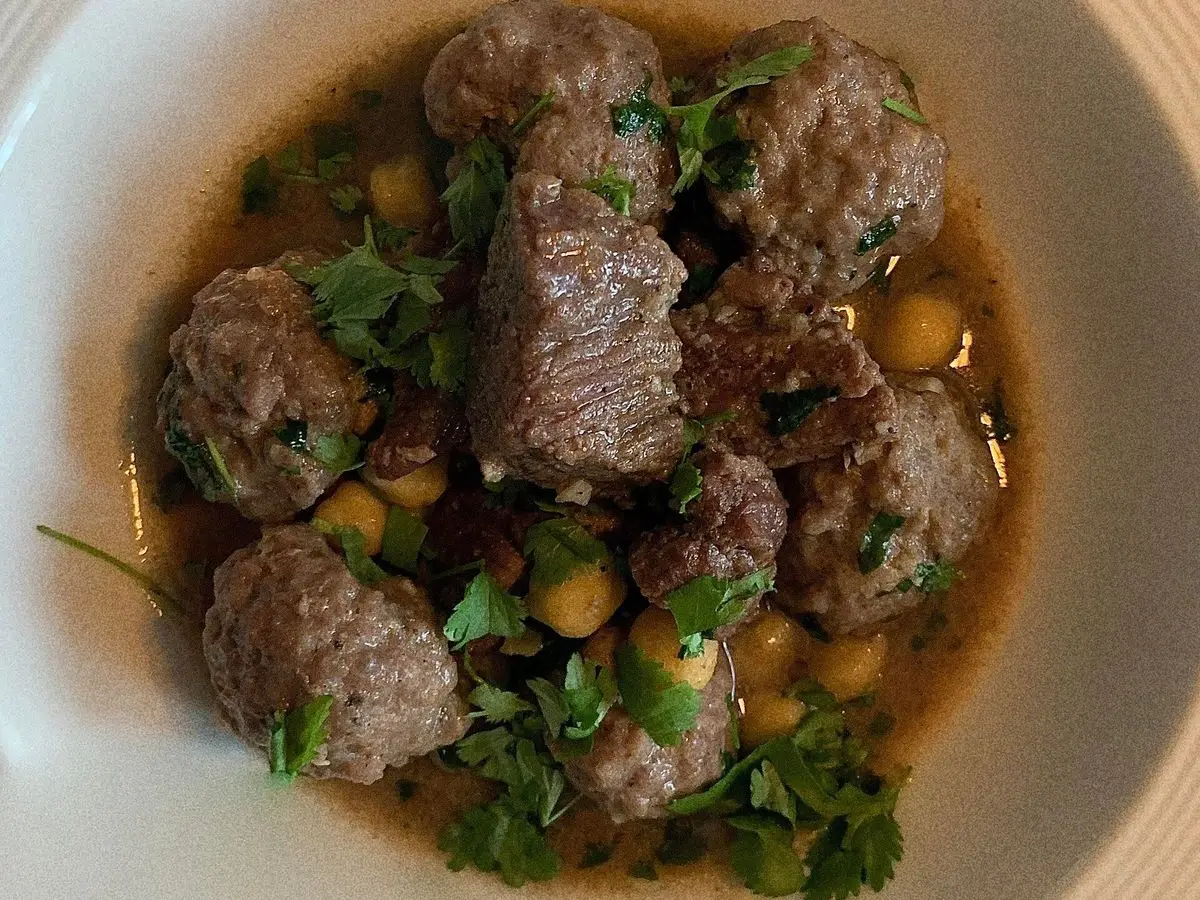 Plato hondo de albóndigas de carne con garbanzos y hierbas frescas en un caldo ligero