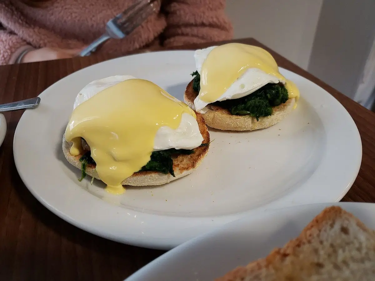 Dos muffins ingleses tostados con espinacas y huevos escalfados en un plato blanco