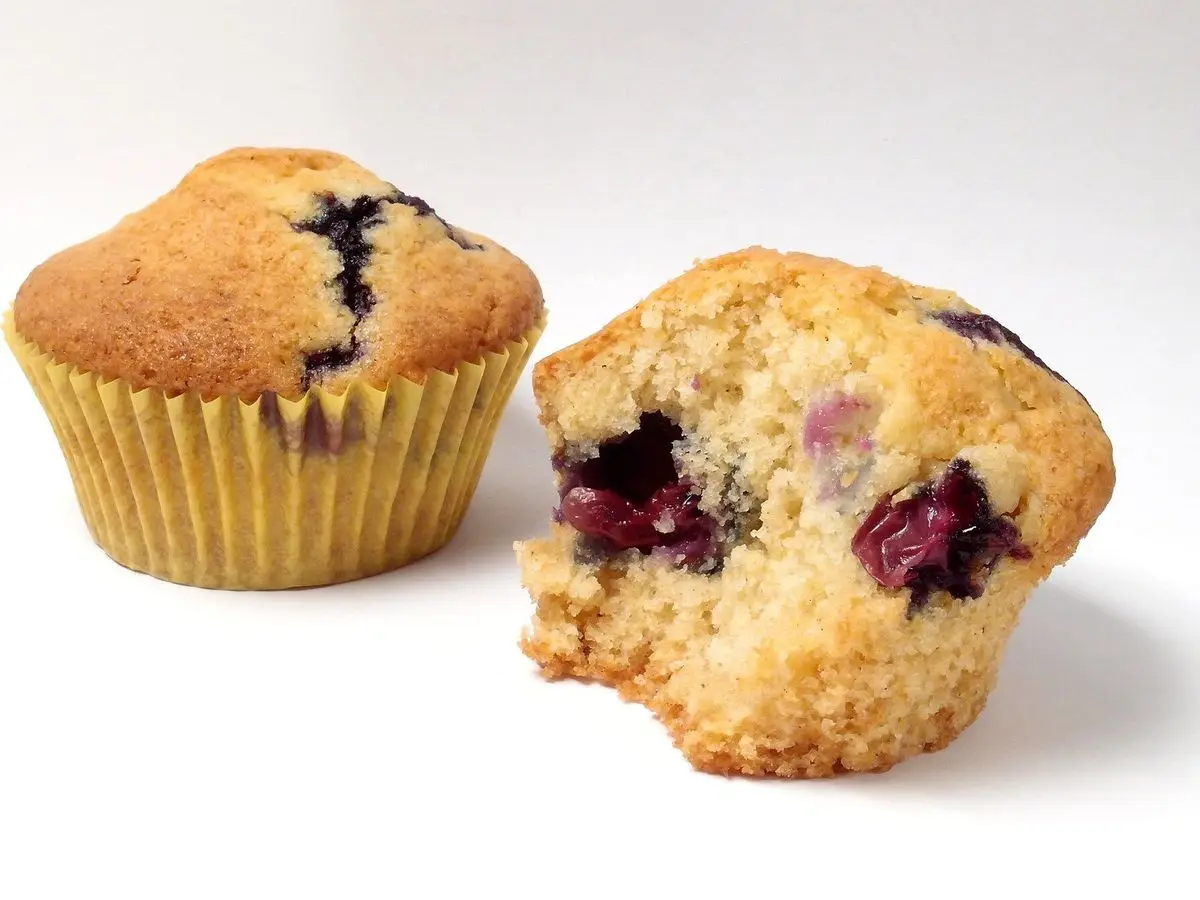 Dos muffins de arándanos, uno entero con su papel y otro partido que muestra los arándanos