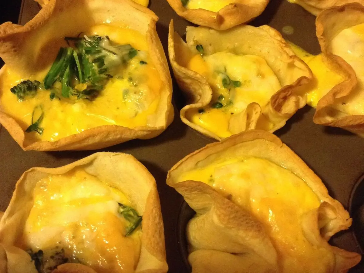 Minitartaletas de huevo y queso doradas con hierbas verdes sobre una bandeja