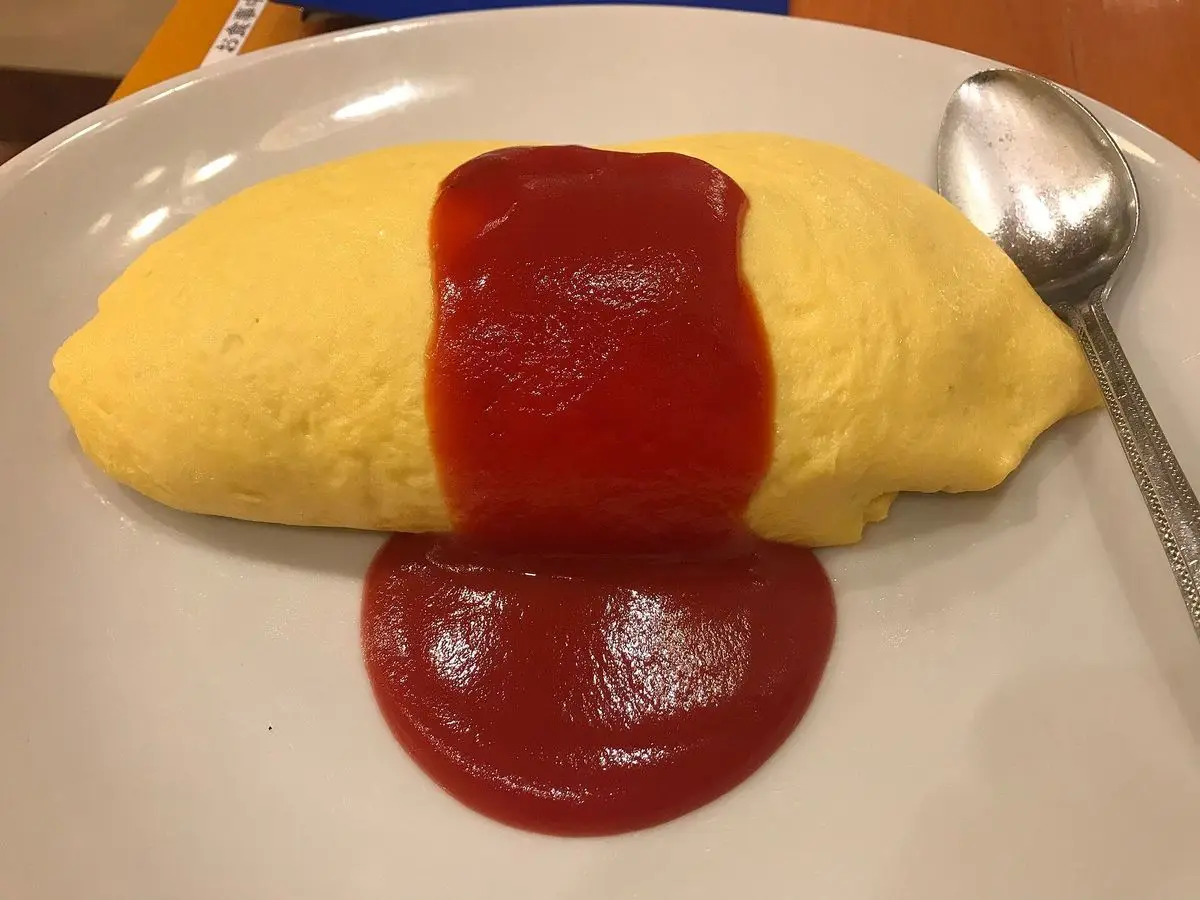 Omelette de arroz amarilla con salsa de tomate roja y una cuchara sobre un plato