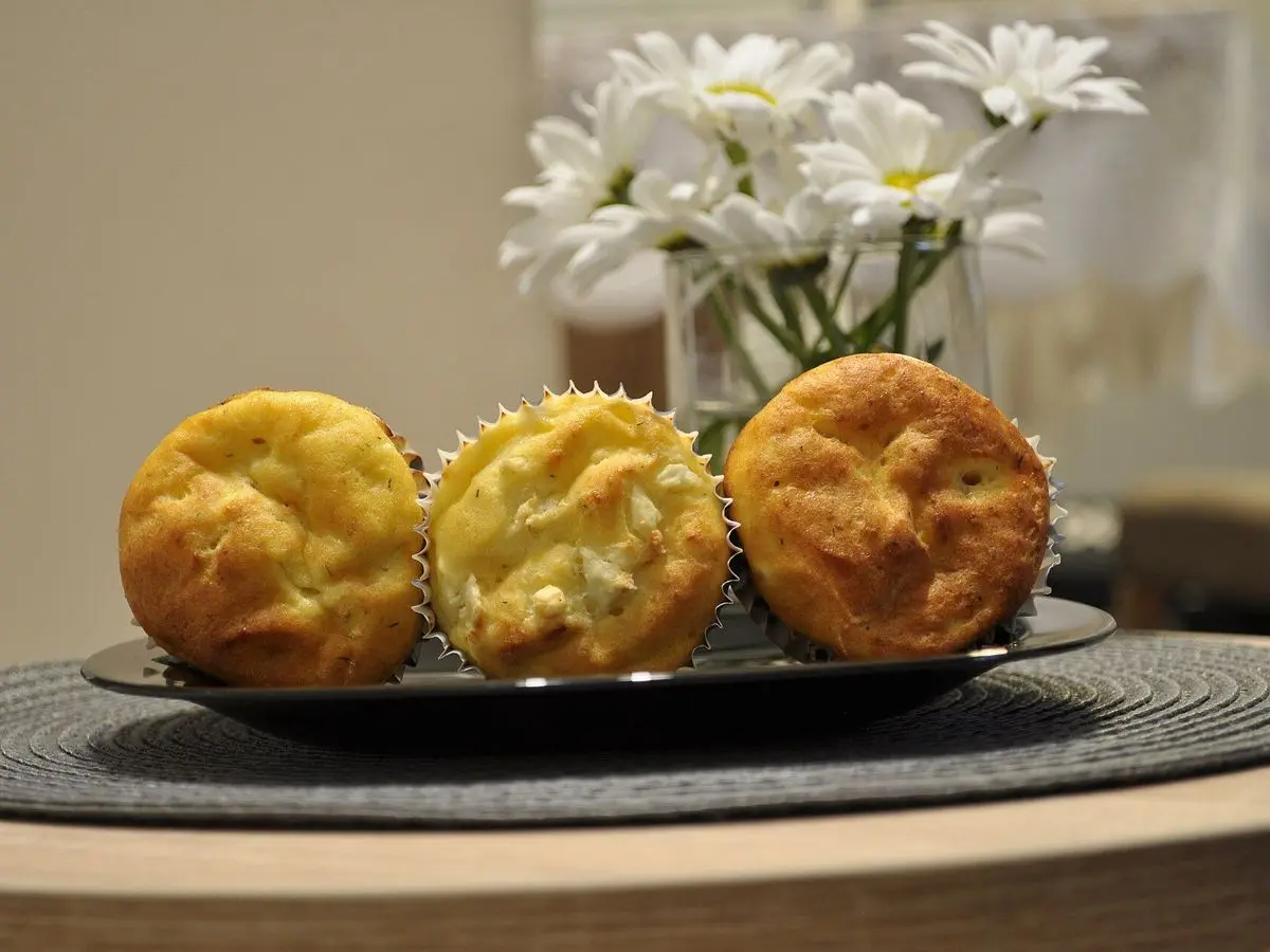 Tres muffins salados dorados sobre una bandeja con un jarrón de flores al fondo