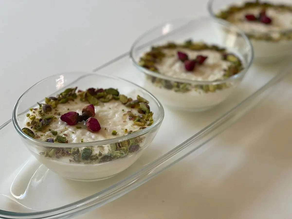 Cuencos de cristal con crema de leche blanca decorada con pistachos picados y pétalos