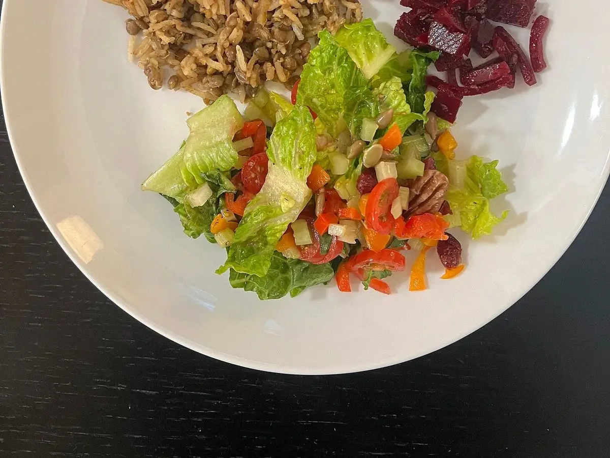 Plato blanco con mujaddara de lentejas y arroz, ensalada de lechuga con pimiento y remolacha troceada