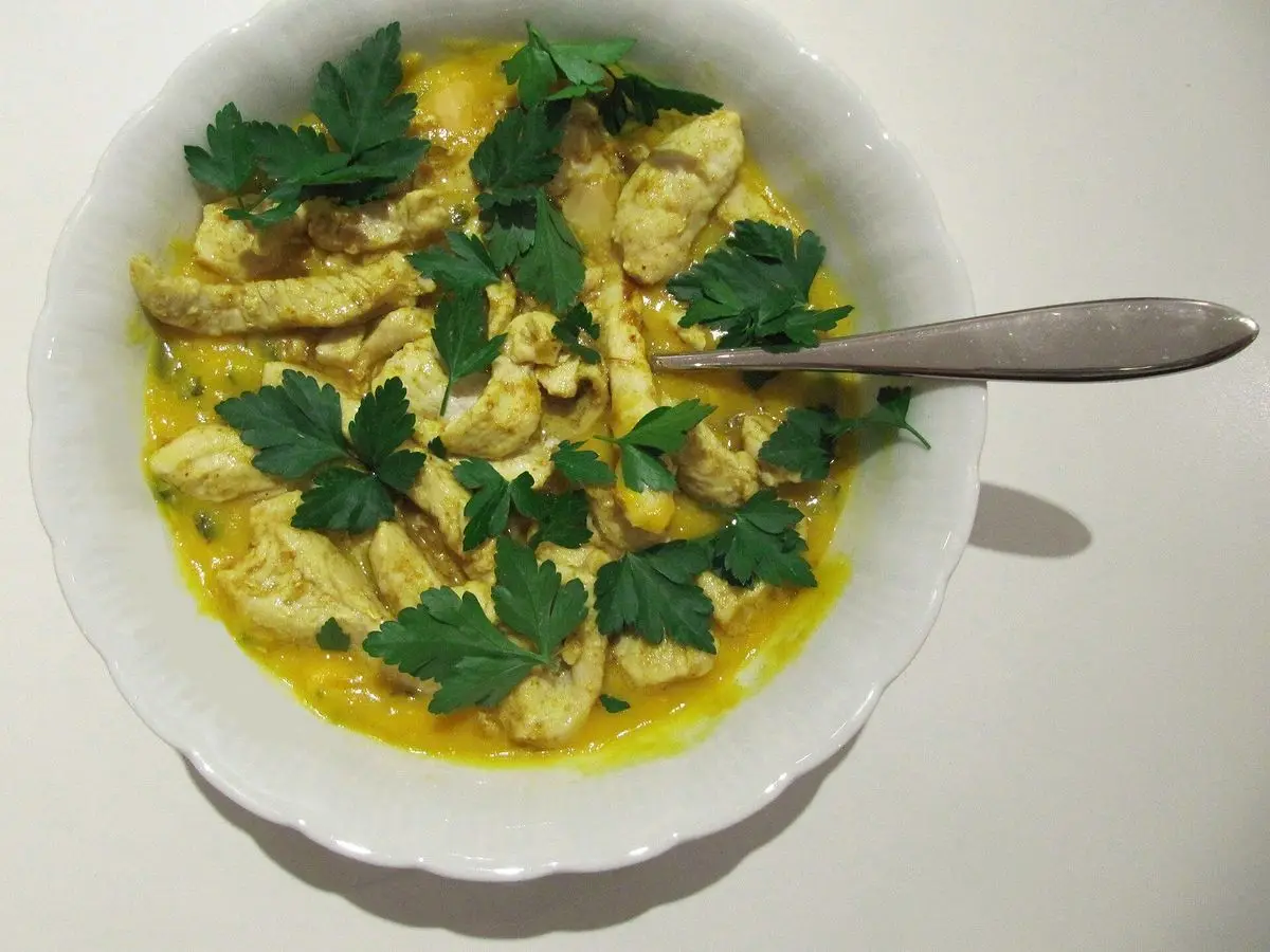 Cuenco blanco de sopa amarilla al curry con tiras de pollo salteado y perejil fresco