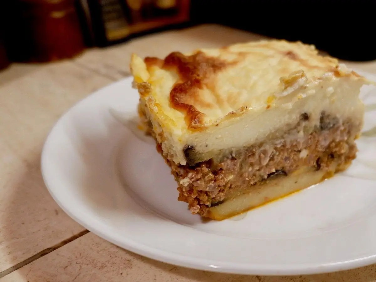 Porción de musaka con carne picada y bechamel gratinada sobre un plato blanco