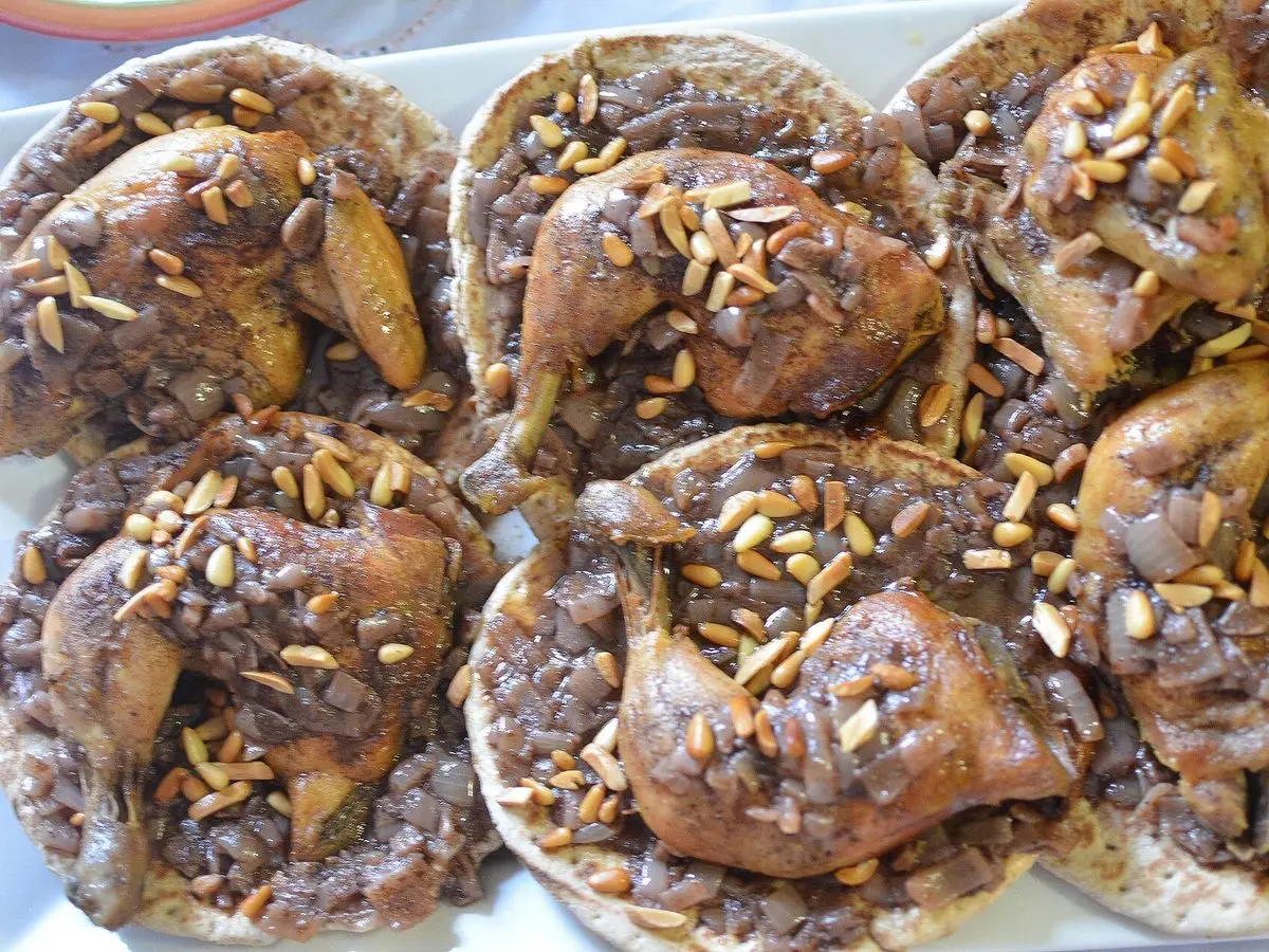 Muslos de pollo asados sobre pan plano con cebolla, zumaque y piñones dorados