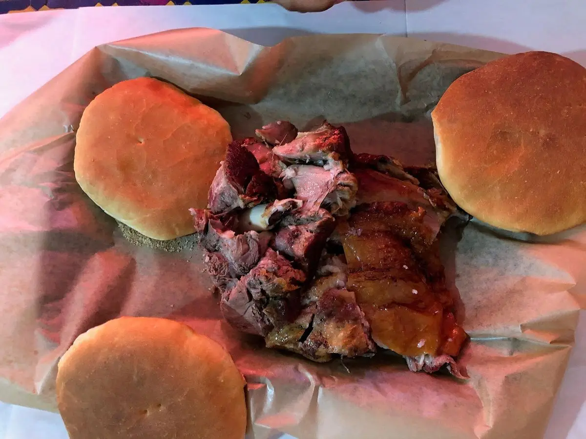 Carne de cordero asada y troceada sobre papel con panecillos redondos a los lados