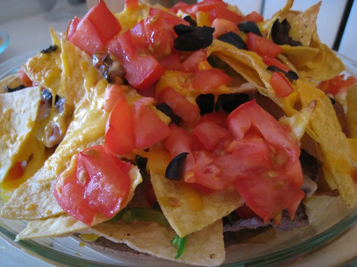 Nachos de maíz cubiertos de queso fundido, tomate en dados y aceitunas negras