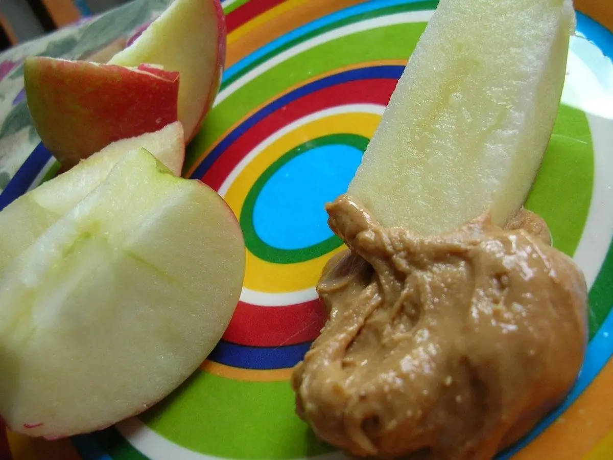 Gajos de manzana roja y verde con crema de cacahuete en un plato de colores
