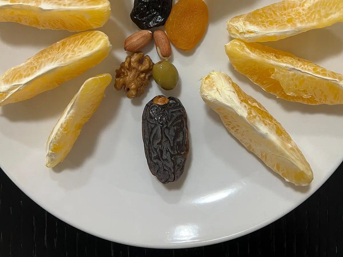 Gajos de naranja dispuestos en círculo con dátiles y frutos secos sobre una mesa blanca