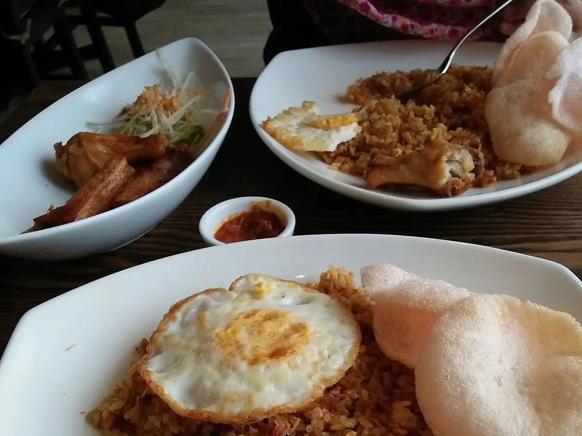 Plato de arroz frito con huevo frito encima, galleta de gambas y rodajas de pepino y zanahoria