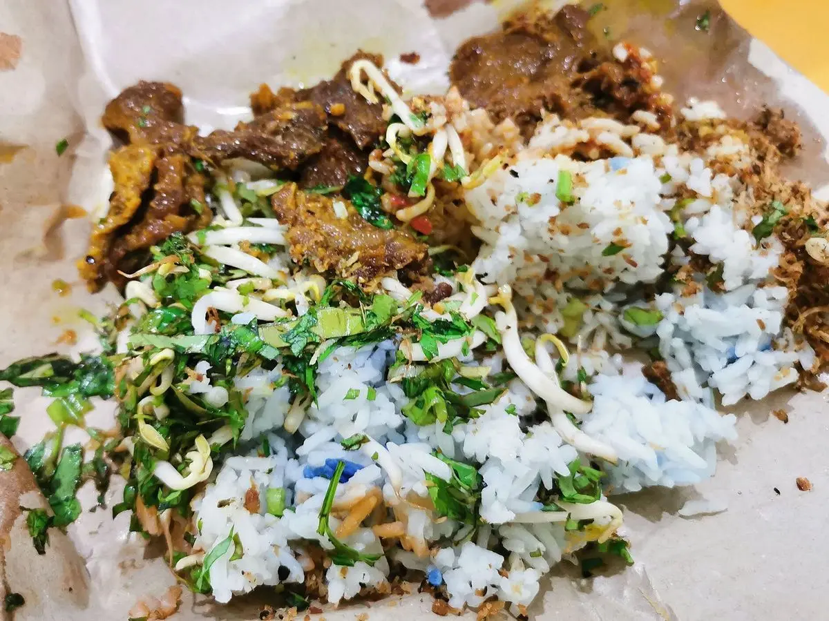 Plato de arroz mezclado con hierbas verdes picadas y carne guisada oscura