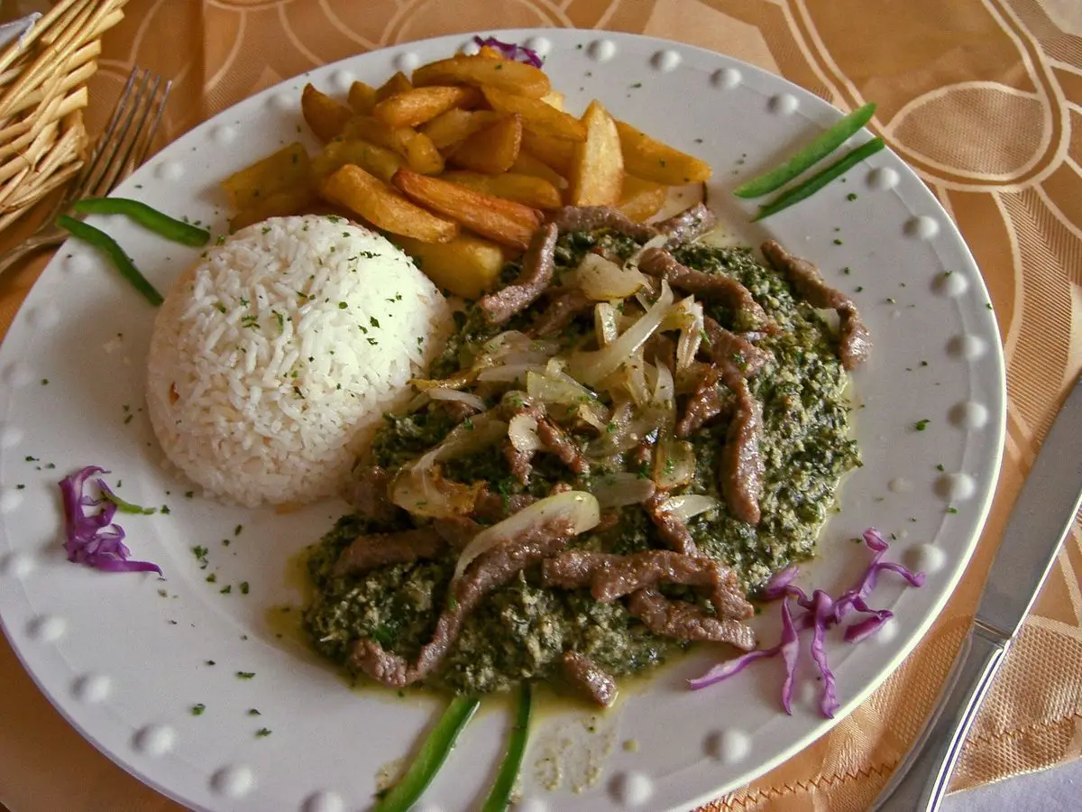 Plato blanco con guiso de hojas verdes y cacahuete, bola de arroz, patatas fritas y cebolla
