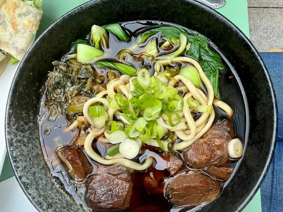 Cuenco de sopa de fideos con trozos de ternera guisada, verduras verdes y cebolleta