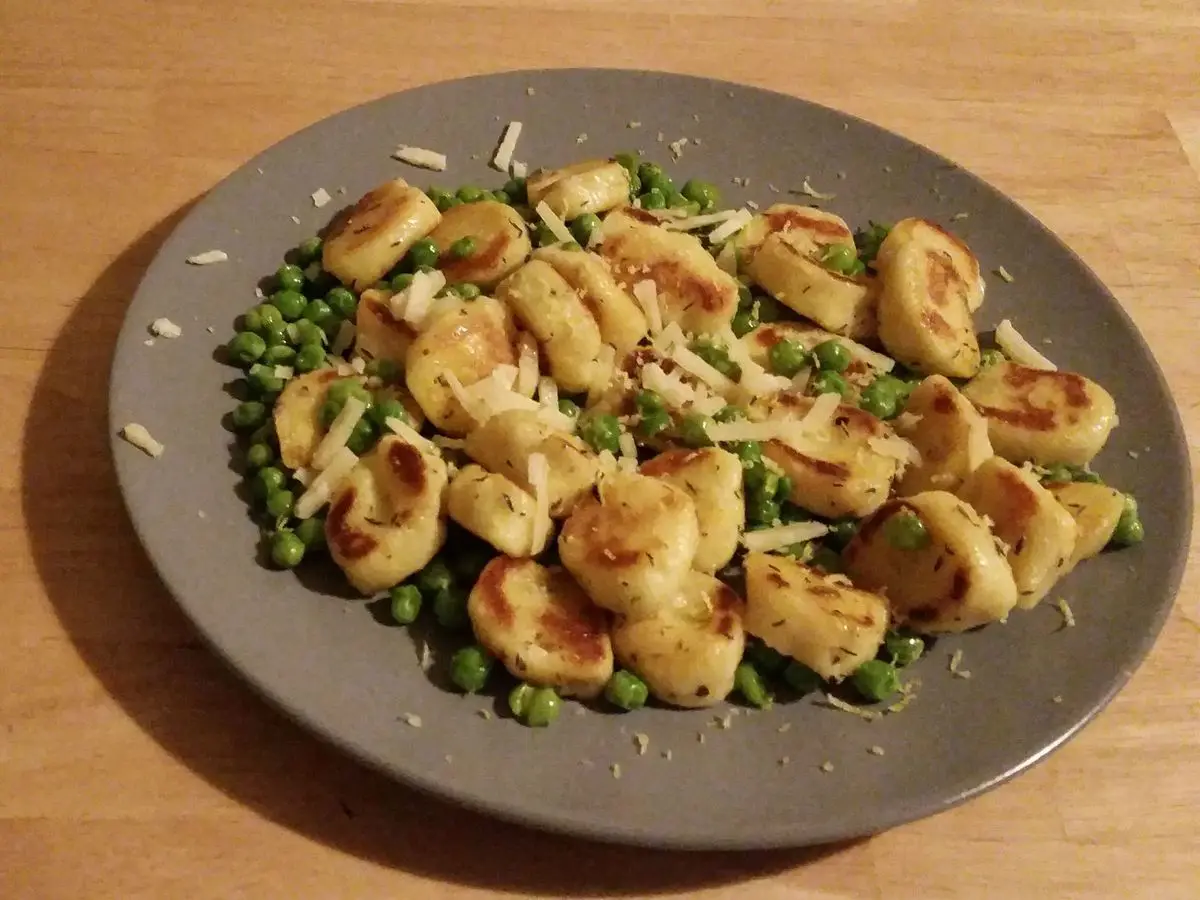 Ñoquis dorados en la sartén con guisantes y parmesano rallado en un plato gris