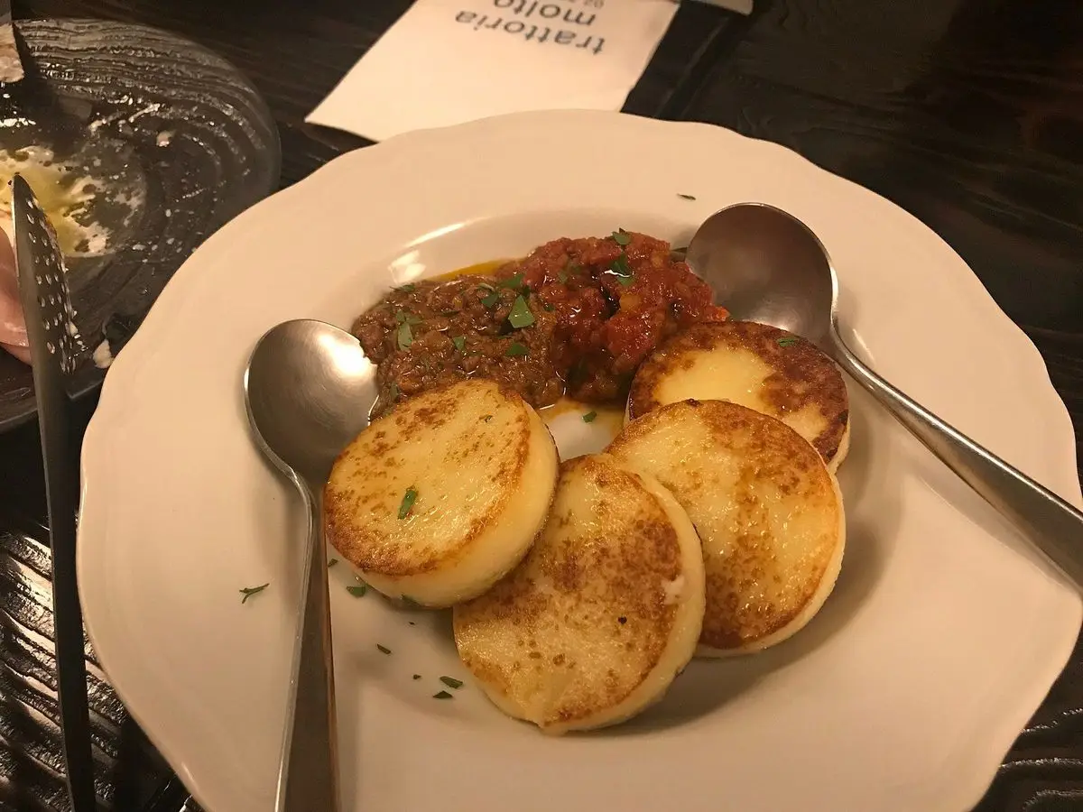 Plato blanco con discos de ñoquis de sémola a la romana y una salsa de tomate al lado
