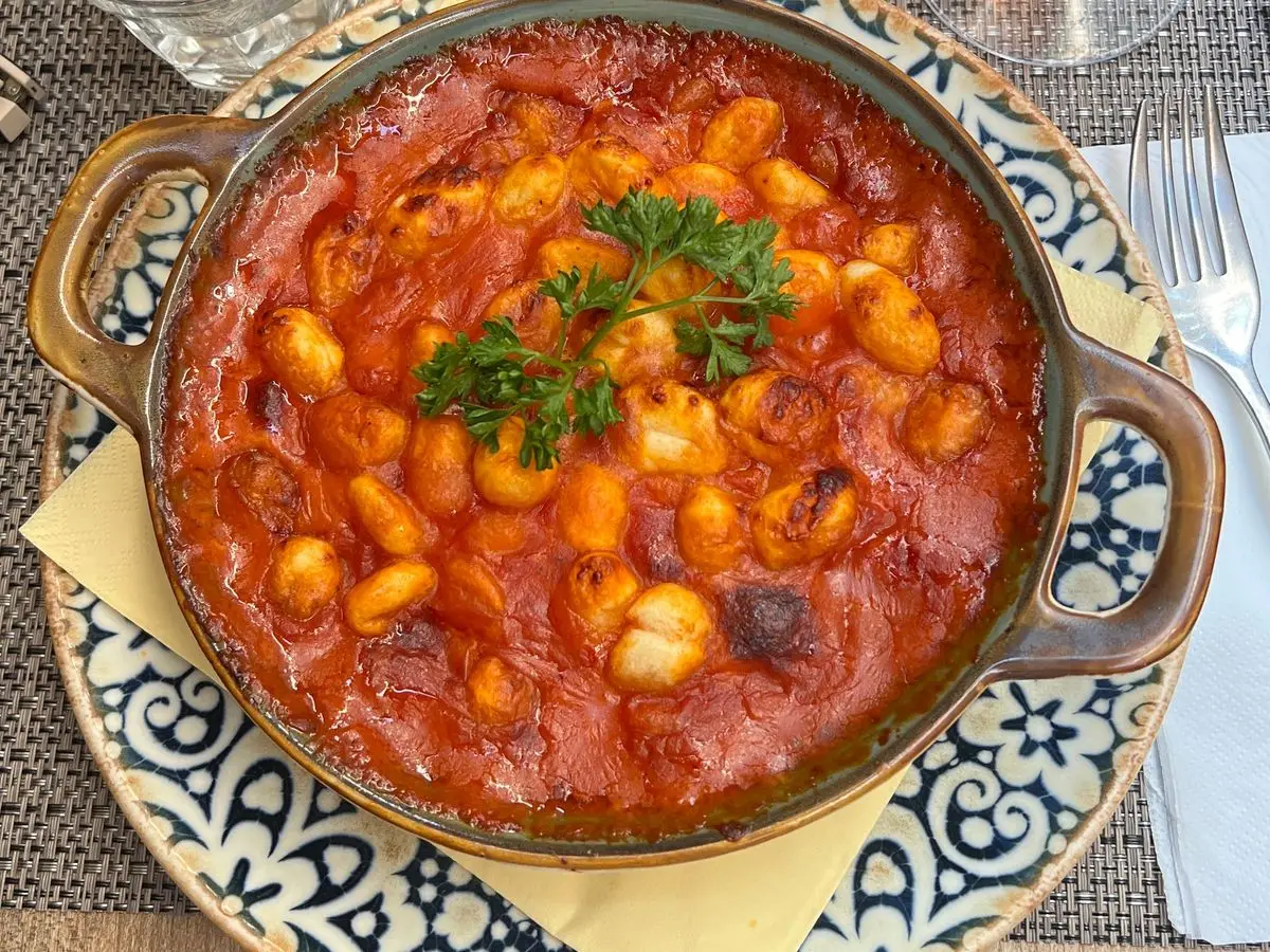 Ñoquis en salsa de tomate con queso fundido y perejil en una cazuela con asas