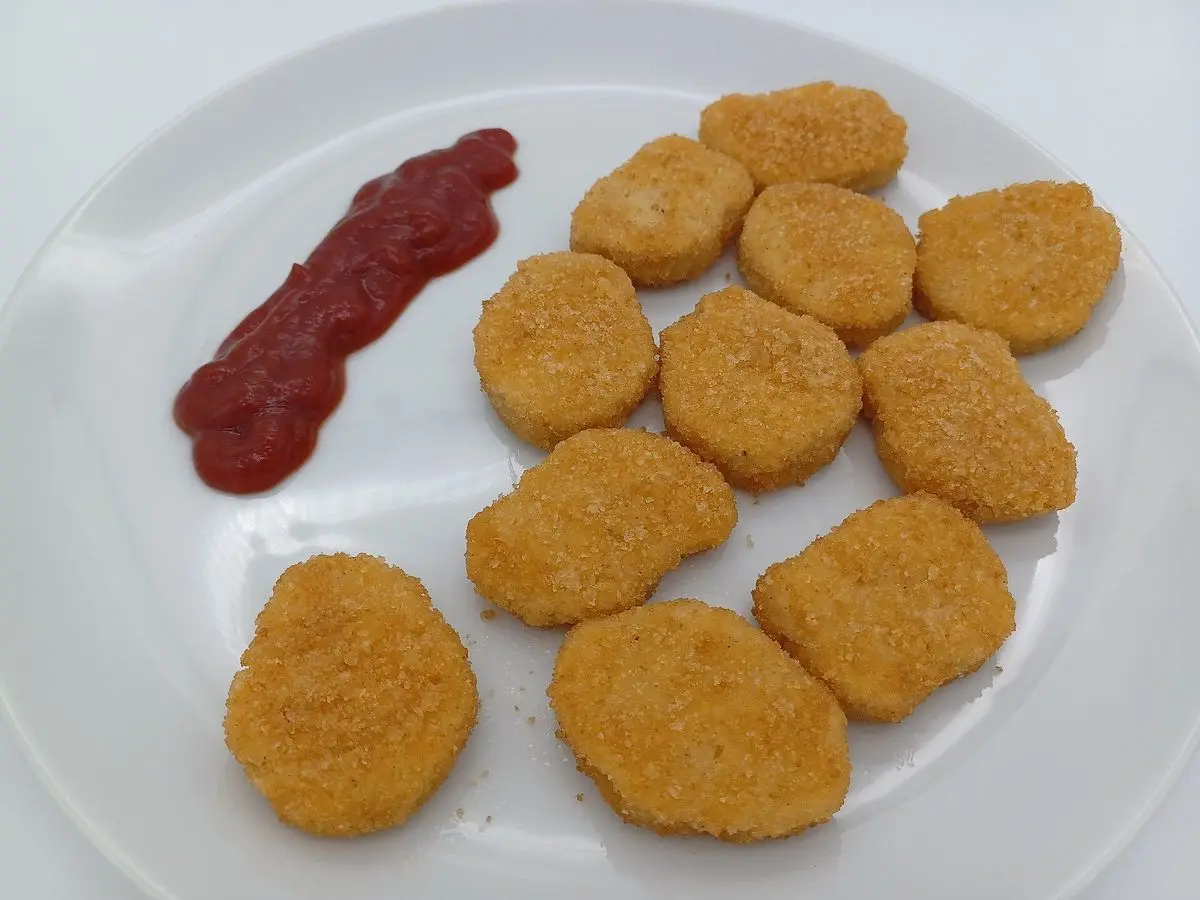 Nuggets dorados de pollo rebozado en un plato blanco con una tira de kétchup
