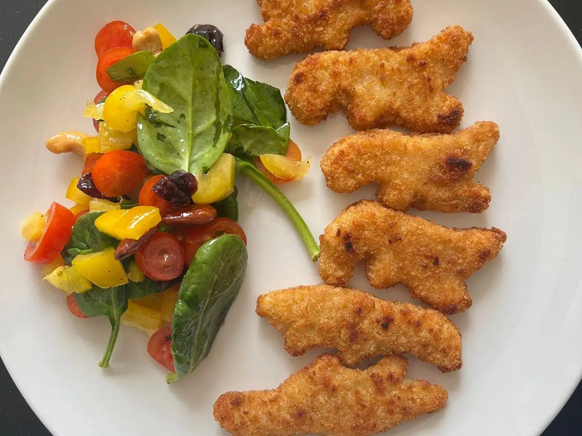 Tiras de pollo empanado con ensalada de espinacas, tomate y pimiento en un plato blanco
