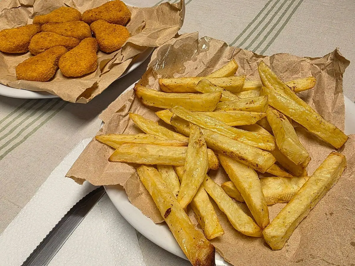 Nuggets de pollo caseros y patatas fritas en bastones sobre papel de estraza