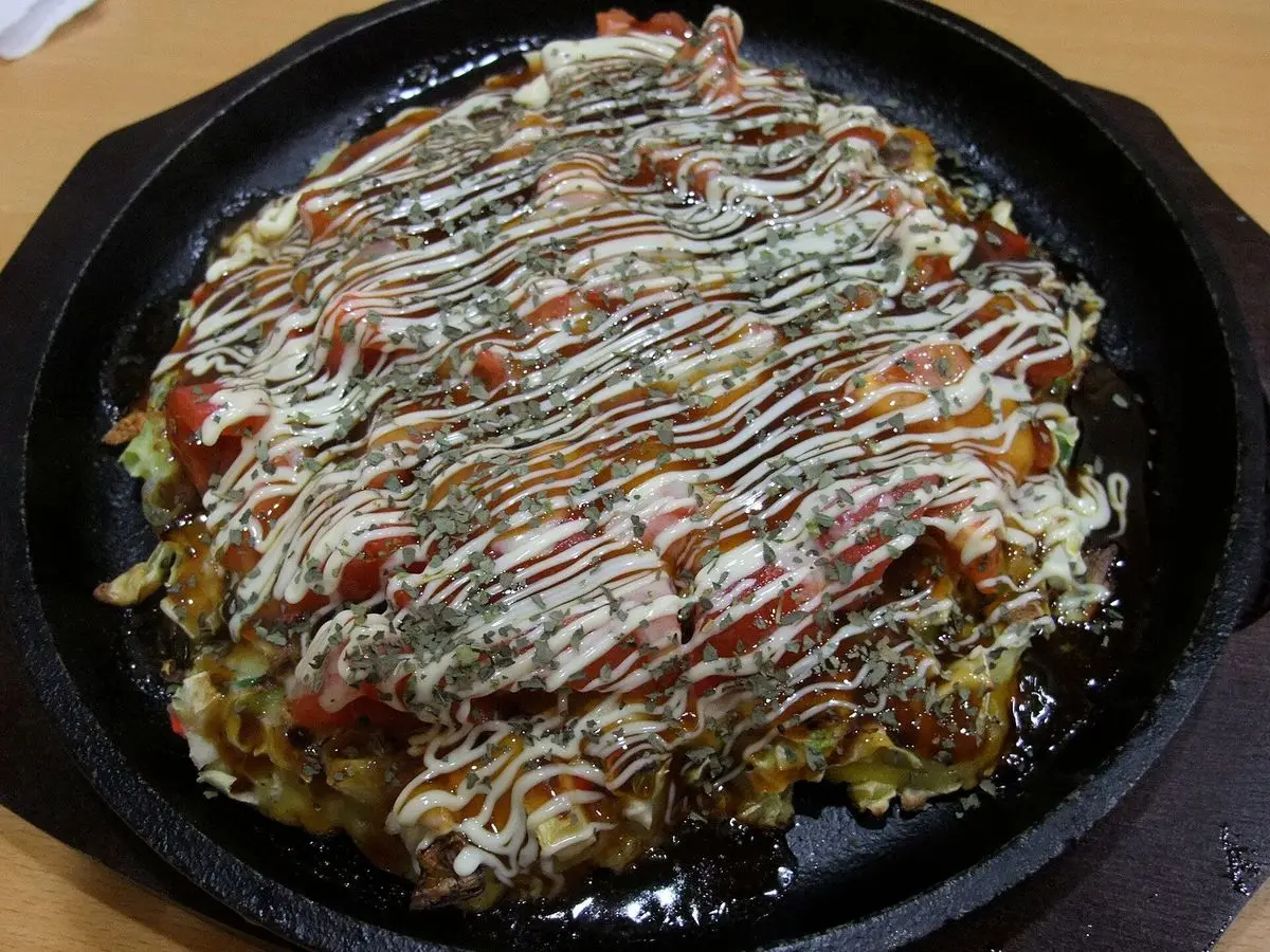 Okonomiyaki con salsa, mayonesa y alga sobre una plancha de hierro negra
