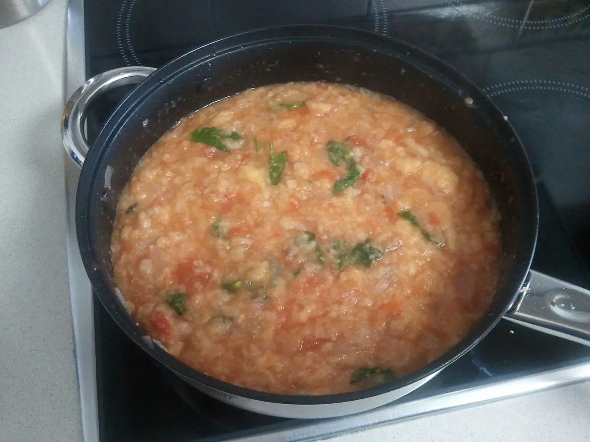 Sartén con sopa espesa de tomate y pan con hojas de hierbabuena, sobre la placa de cocina