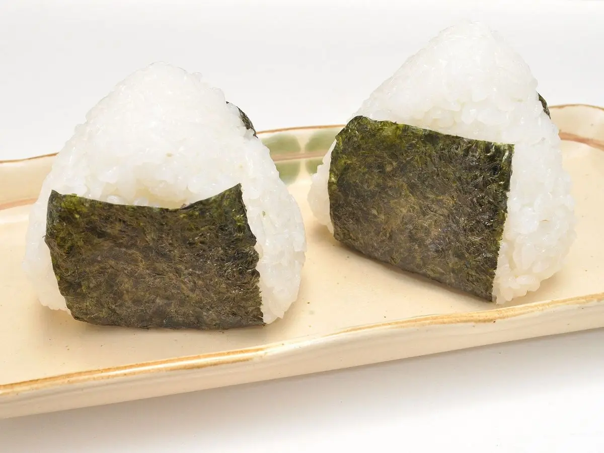 Dos onigiris triangulares de arroz blanco envueltos en alga nori sobre una bandeja