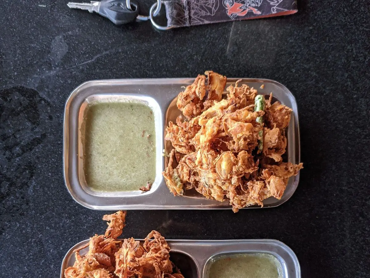 Bandejas metálicas con onion bhaji crujientes y chutney verde de cilantro y yogur para mojar