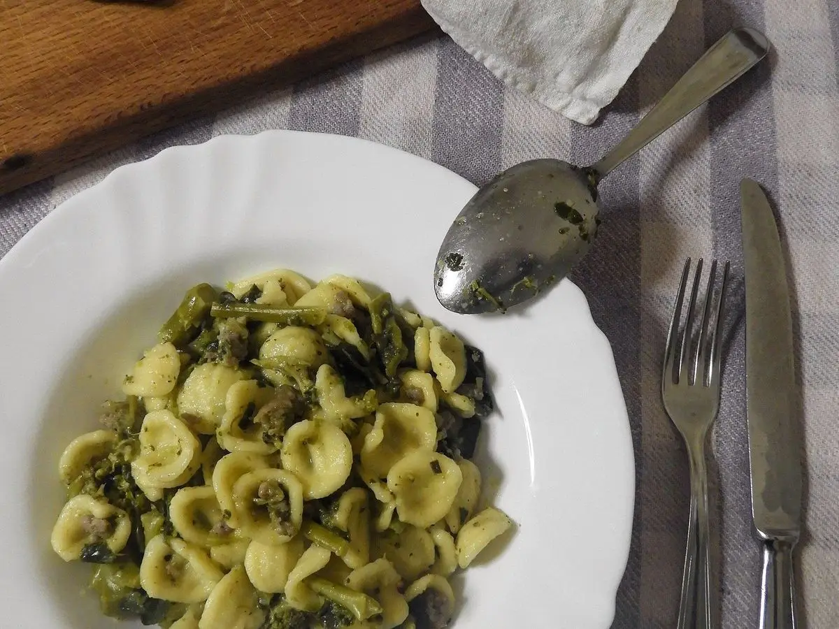 Plato blanco de orecchiette con brócoli salteado junto a cubiertos sobre un mantel de cuadros