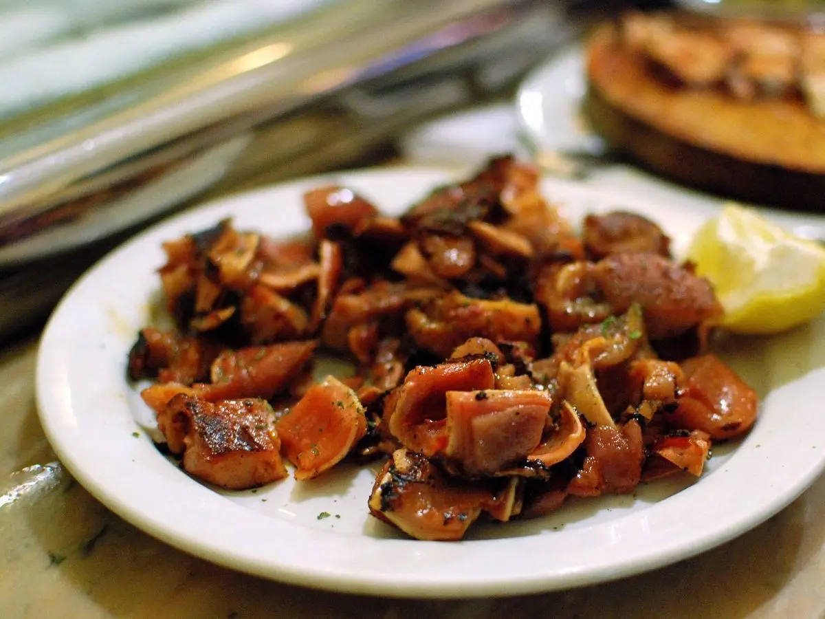 Plato blanco con trozos de oreja de cerdo dorados y rojizos y una cuña de limón en un bar de tapas