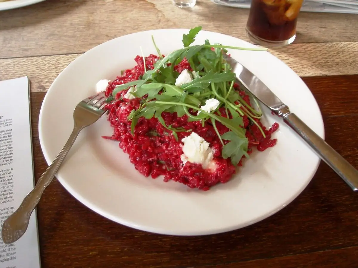 Risotto rosado de remolacha con queso de cabra desmenuzado y hojas de rúcula en un plato blanco