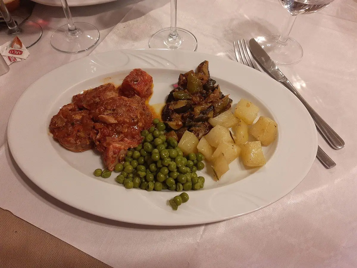 Plato blanco con osobuco de ternera, guisantes, patatas cocidas y verdura salteada