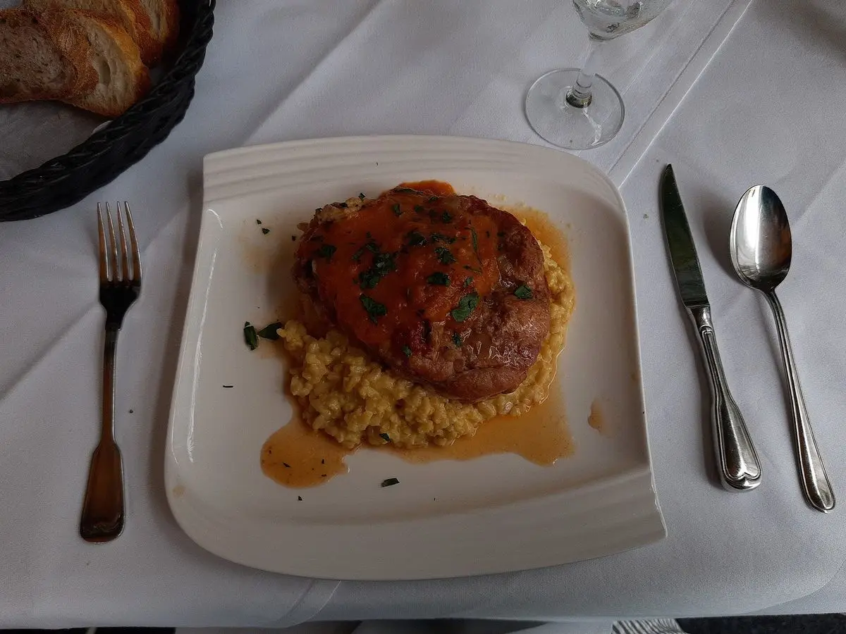 Ossobuco de ternera con salsa sobre una base amarilla cremosa en un plato cuadrado blanco