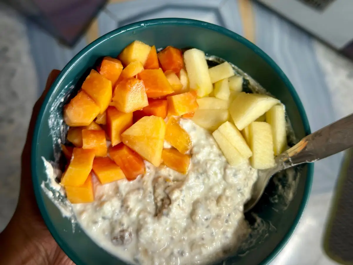 Cuenco verde de avena remojada con dados de fruta naranja y amarilla por encima