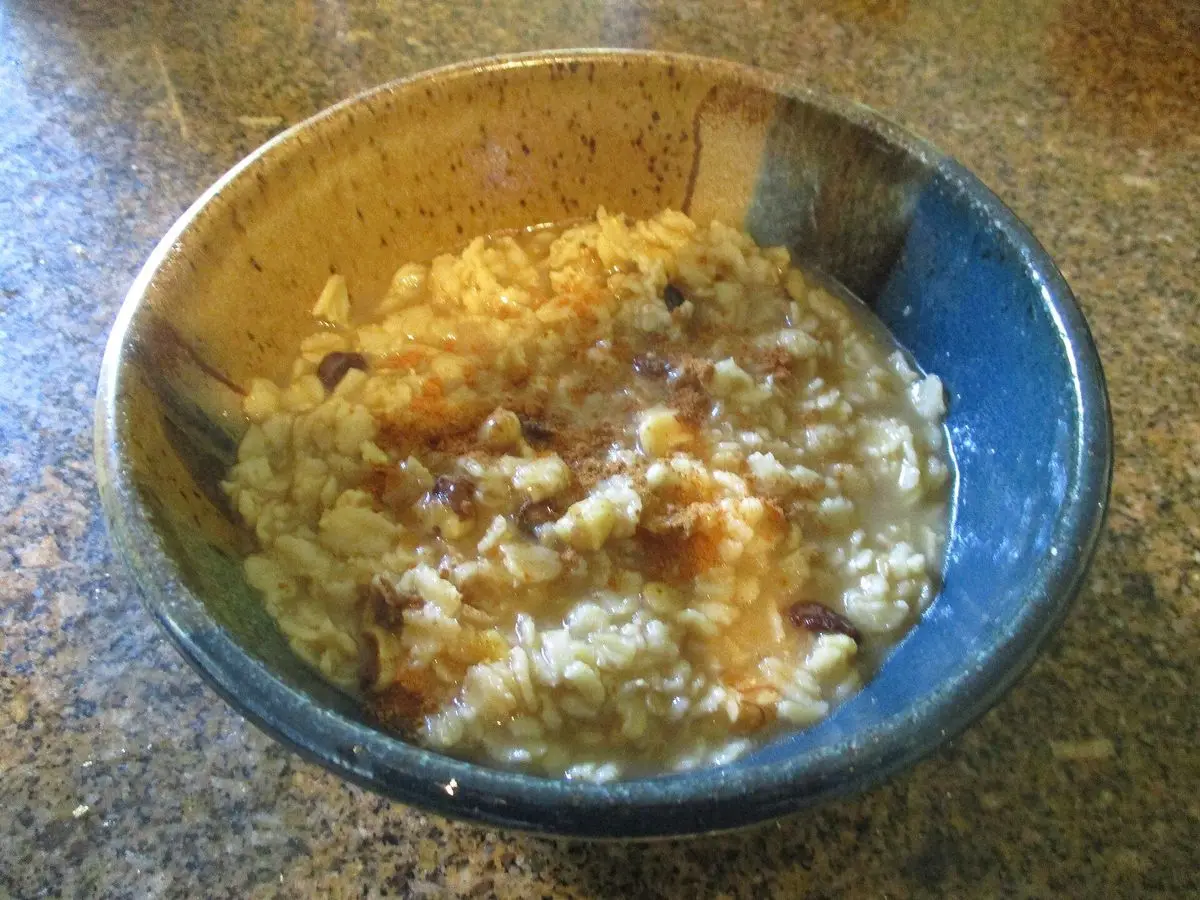 Cuenco de cerámica azul con copos de avena en leche, pasas y canela espolvoreada por encima