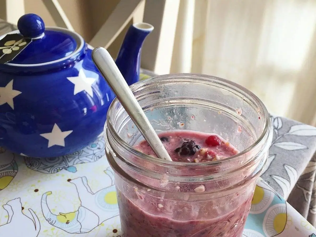 Tarro de cristal con avena cremosa y compota morada de fruta con una cuchara sobre un mantel de lunares