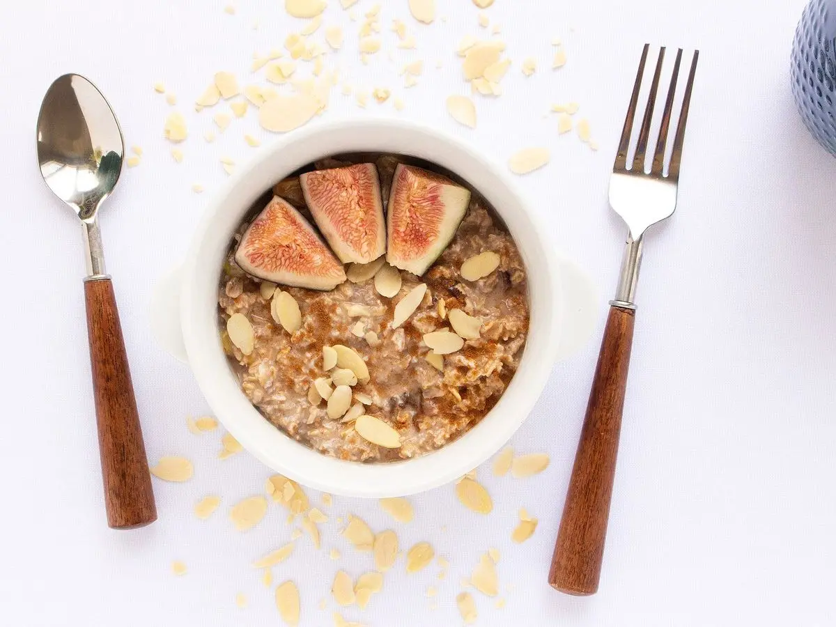 Cuenco de avena con higos frescos partidos y copos de almendra, con cuchara y tenedor
