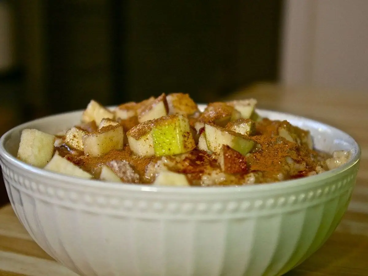 Cuenco blanco de avena cubierta de manzana en dados espolvoreada con canela