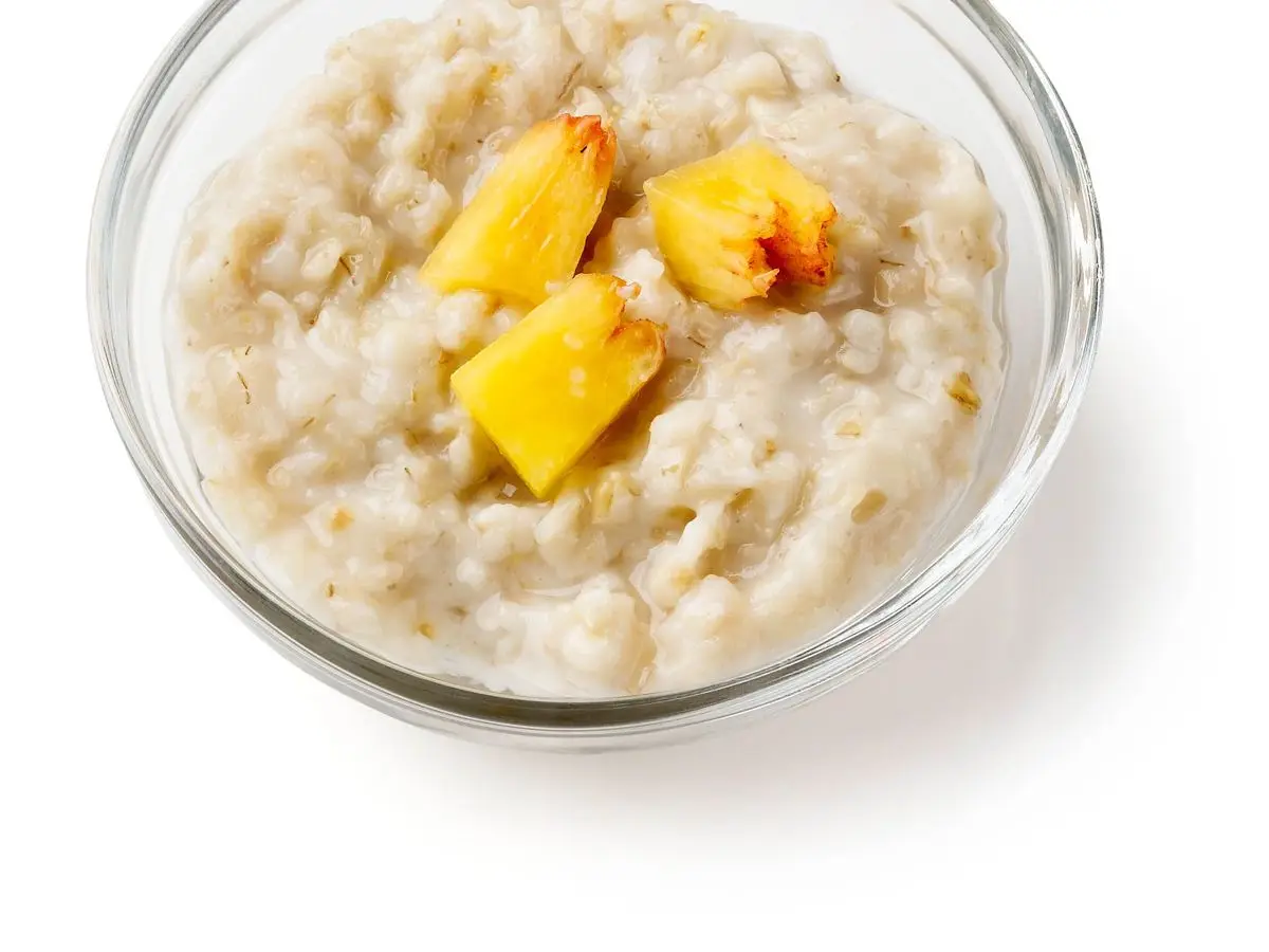 Cuenco de cristal con avena cremosa y trozos de melocotón sobre fondo blanco