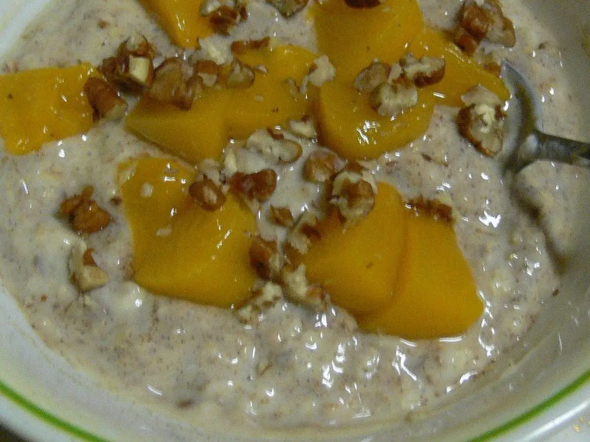 Avena cremosa en un cuenco con trozos de fruta amarilla y frutos secos picados por encima