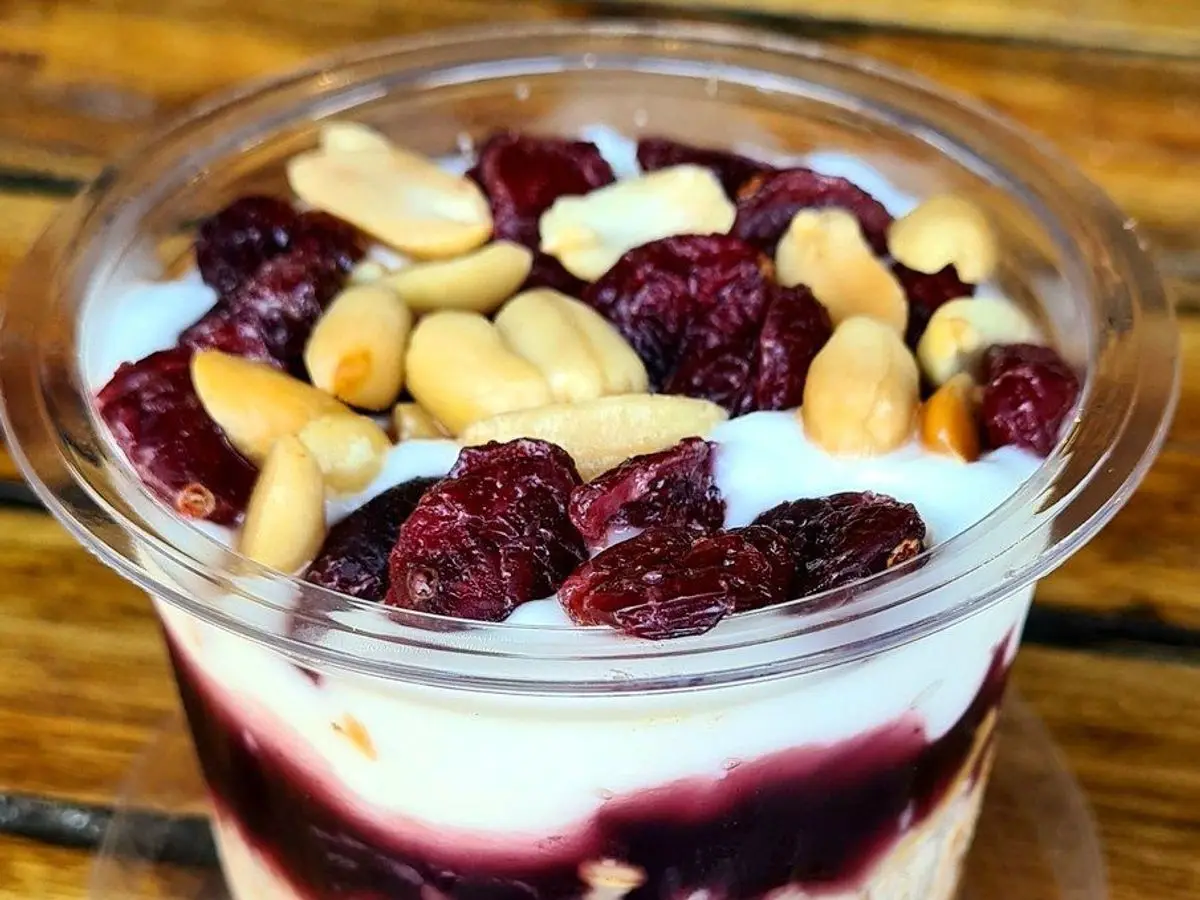 Vaso con capas de avena, yogur y compota de frutos rojos coronado con arándanos y frutos secos