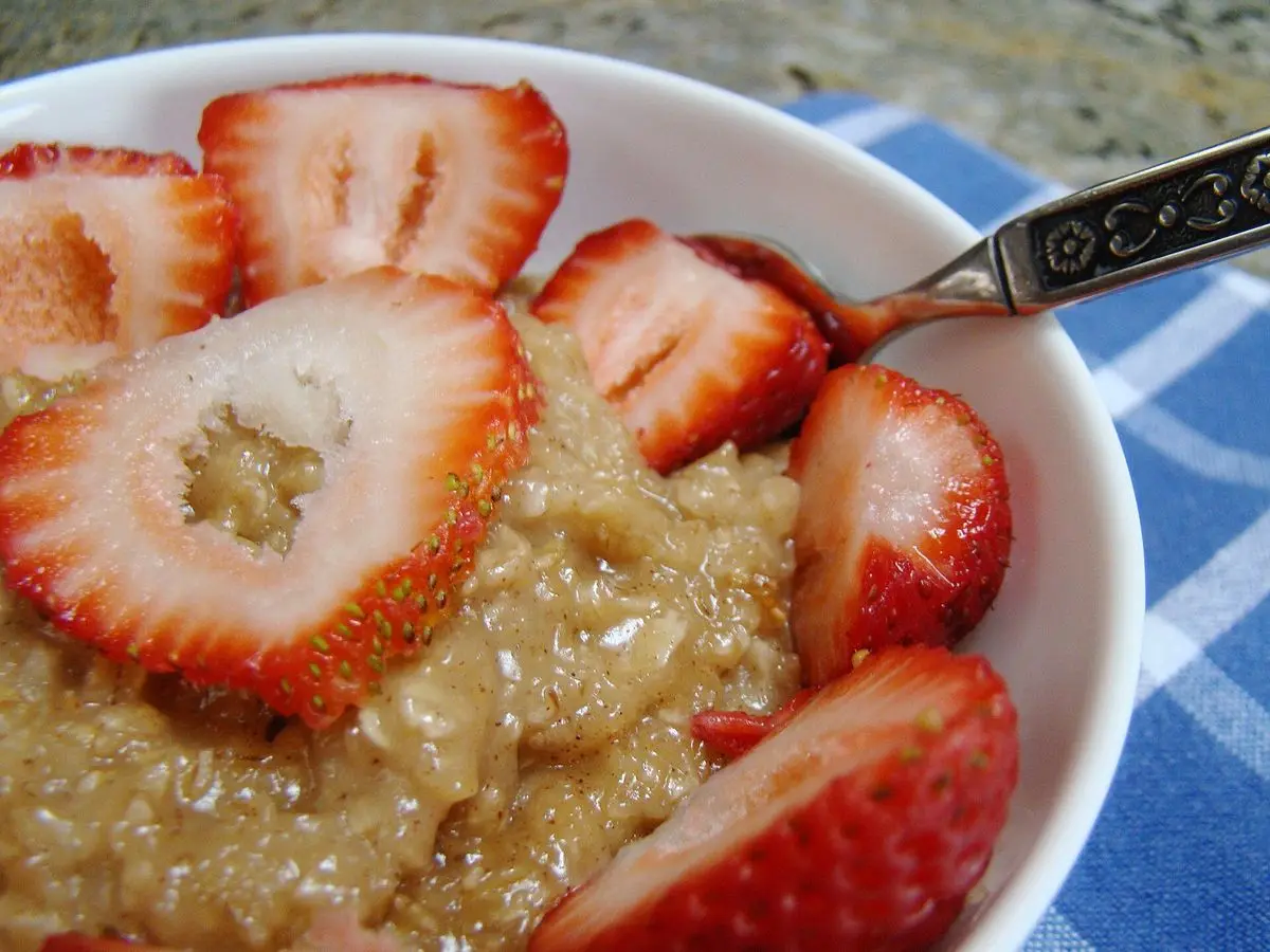 Cuenco blanco de avena cocida cubierto de fresas laminadas sobre un mantel azul de cuadros