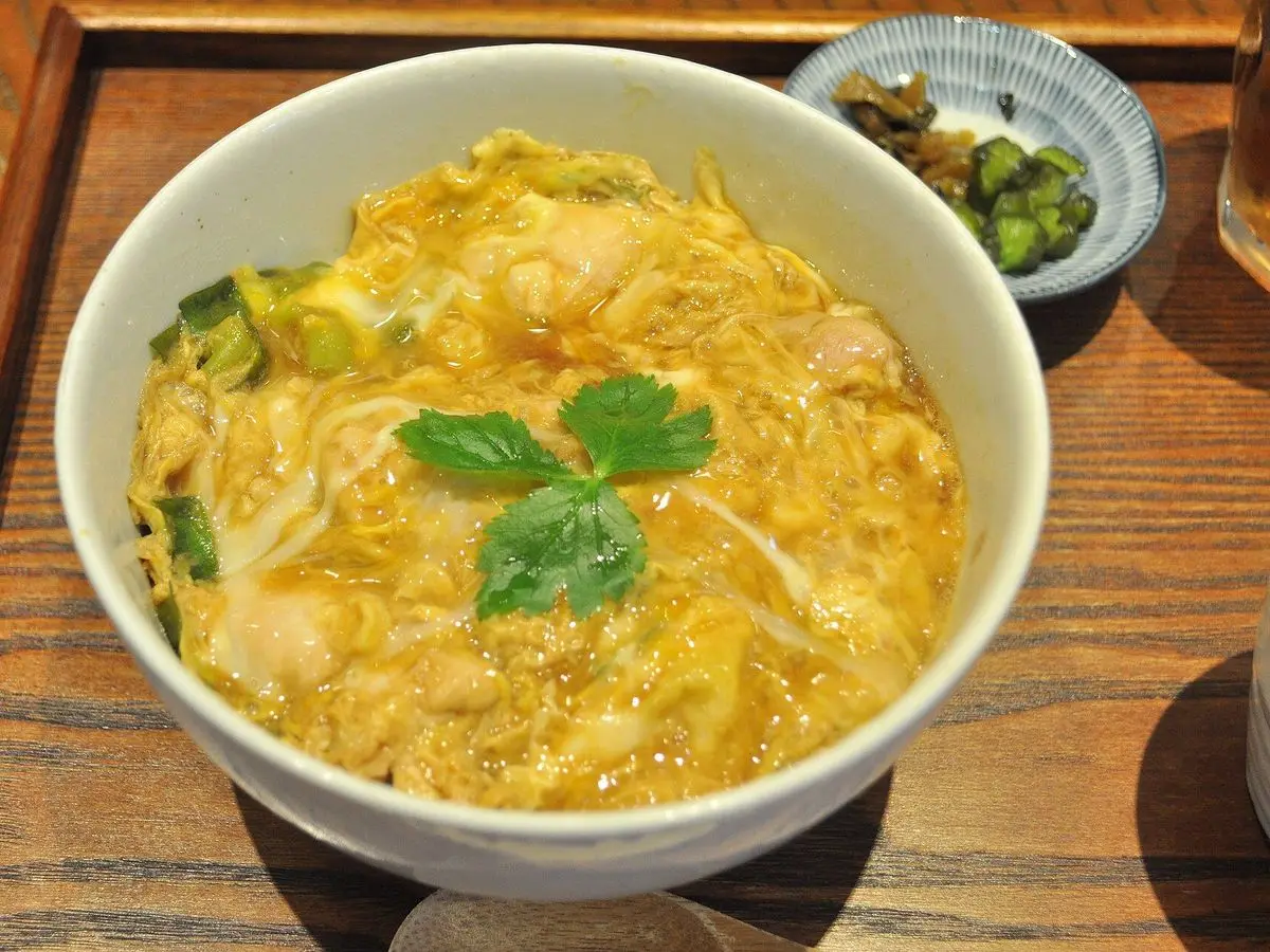 Cuenco de oyakodon con pollo y huevo cuajado y hojas de mitsuba sobre arroz, con encurtidos al lado