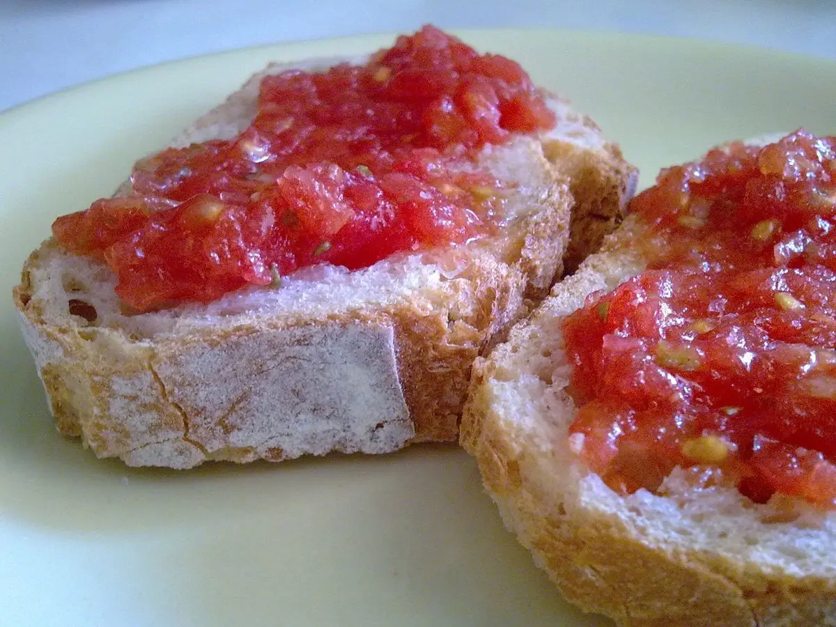 Dos rebanadas de pan rústico con tomate rallado y aceite sobre un plato blanco