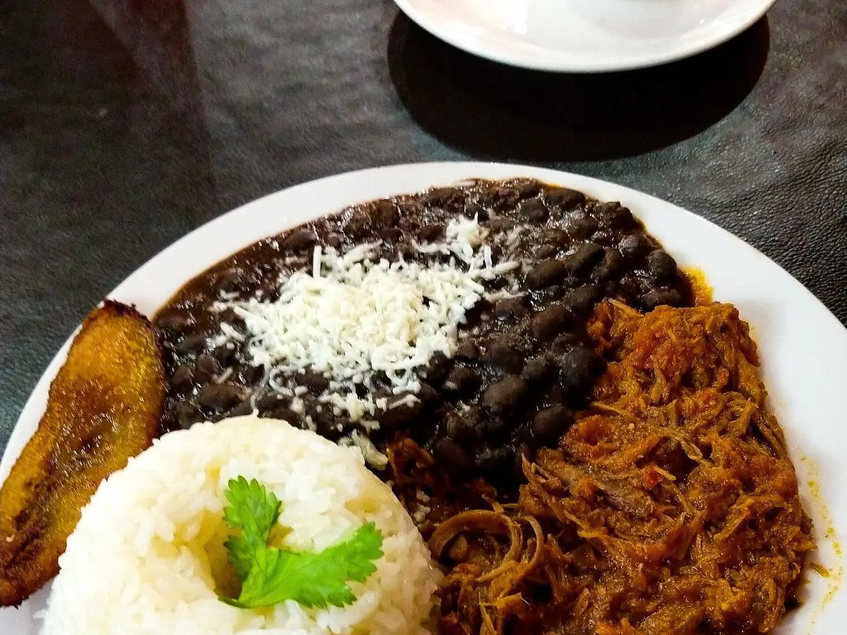 Plato de pabellón criollo con alubias negras y queso rallado, carne mechada, arroz blanco y plátano frito