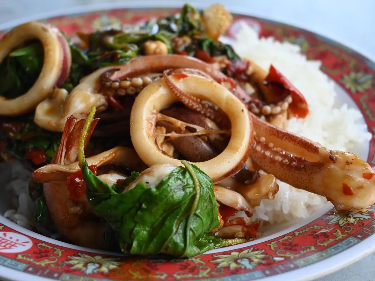 Plato de anillas y tentáculos de calamar salteados con hojas de albahaca y guindilla sobre arroz